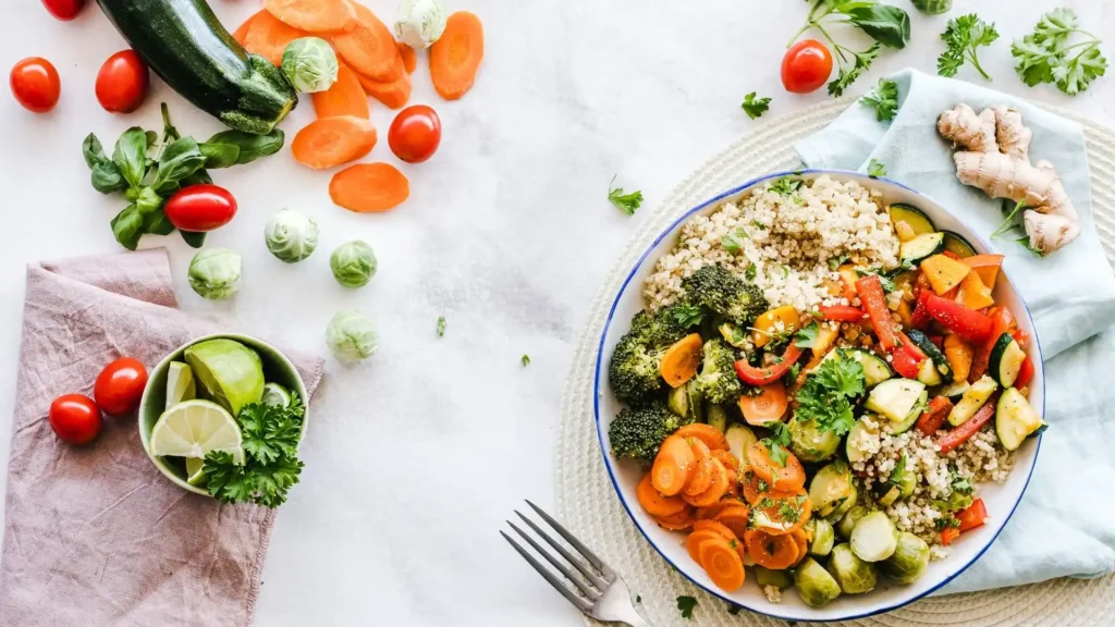 Asian-inspired quinoa bowl with roasted vegetables including carrots, broccoli, brussels sprouts and zucchini, served with fresh herbs and lime wedges