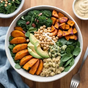 A vibrant Buddha bowl with quinoa, roasted sweet potatoes, broccoli, avocado slices, chickpeas, spinach, and a drizzle of tahini dressing, served on a wooden table with a side of dressing.